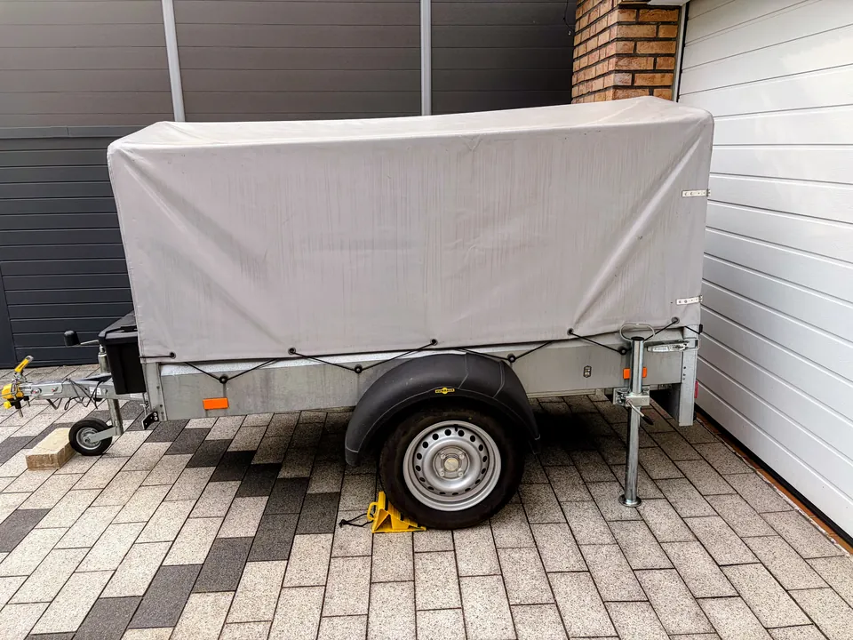 Der Humbaur-Anhänger mit geschlossener grauer Hochplane in der Seitenansicht; Rad, Kotflügel und Deichsel sind sichtbar.